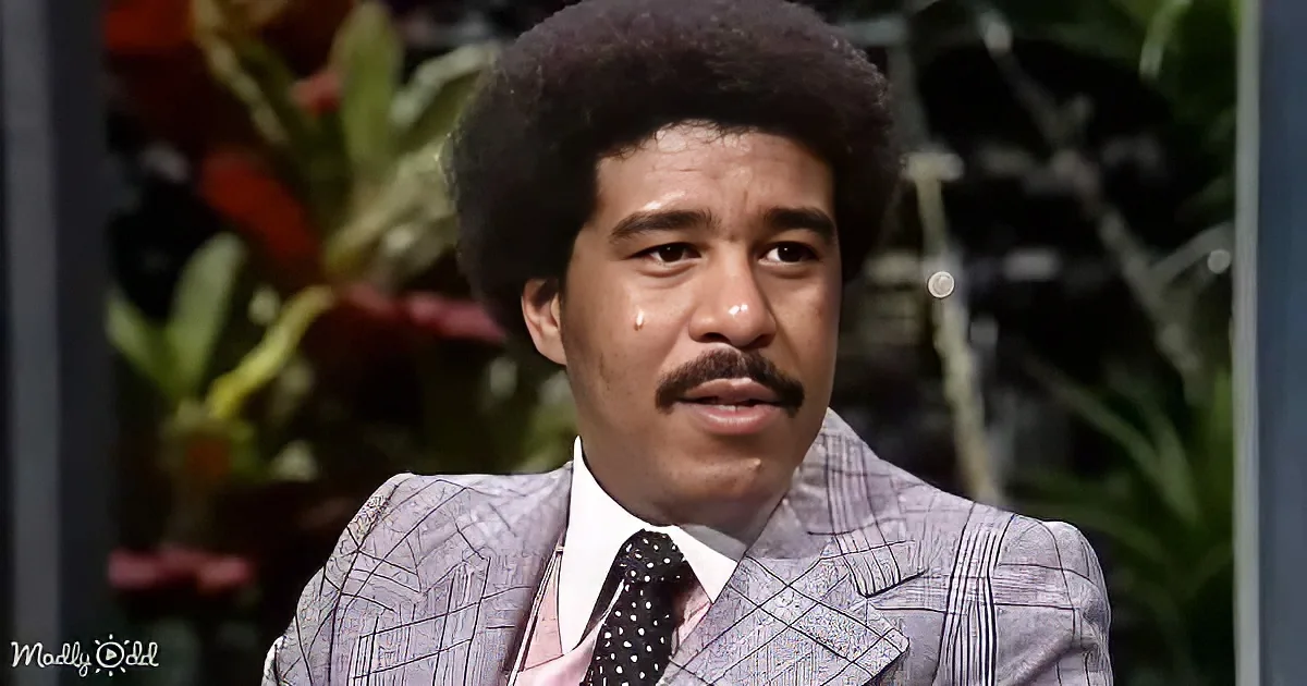 A man with a large afro, mustache, and suit is crying, with a blurred background of plants.