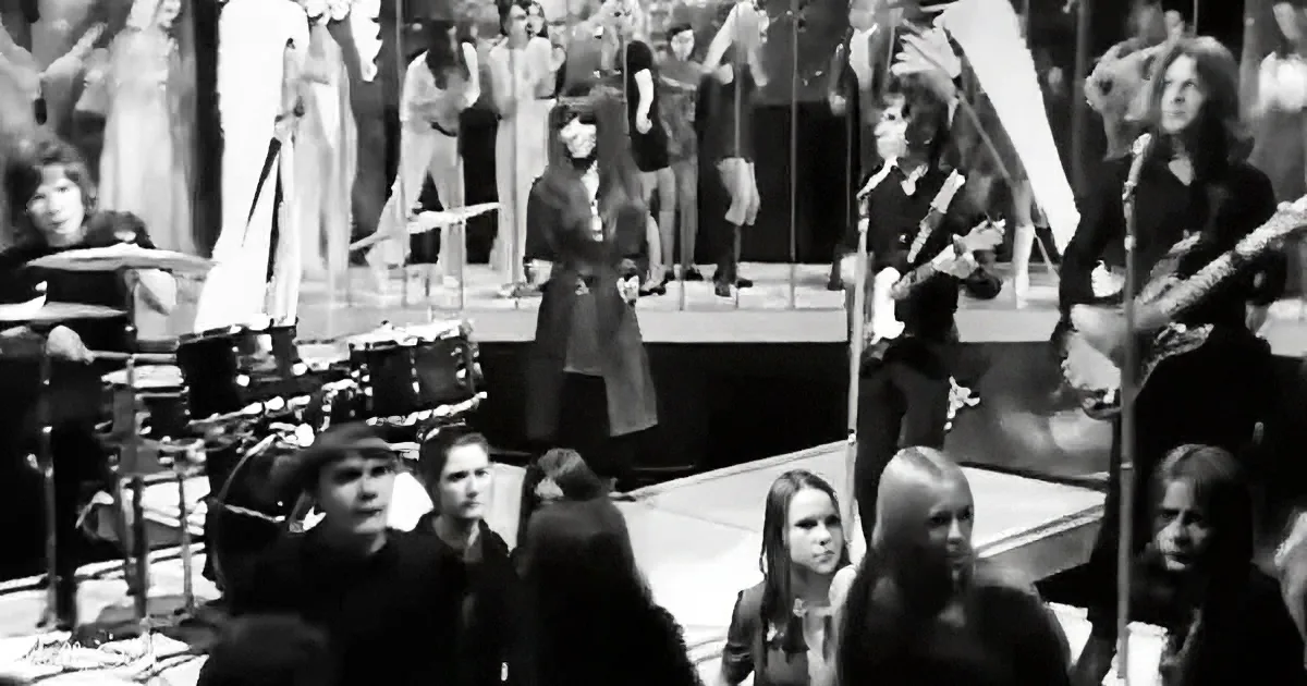 A band performs on stage with a crowd watching, in a black-and-white image.