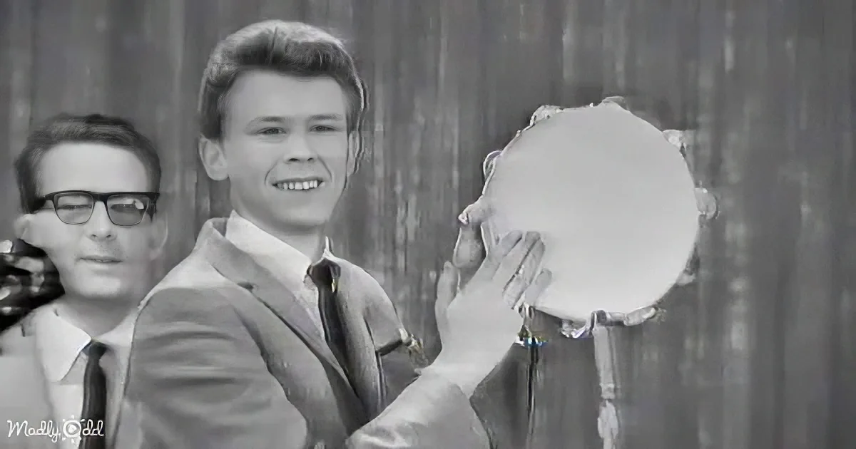 A man in a suit smiles while holding a white object, with another person in the background.