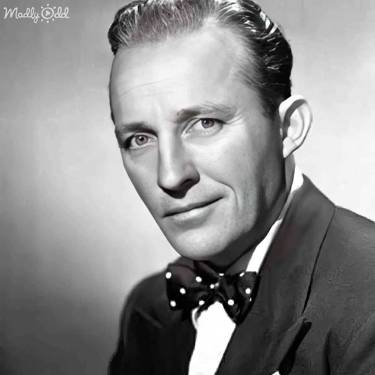 A man in a suit and bow tie, smiling, with neatly combed hair, in a black-and-white portrait.