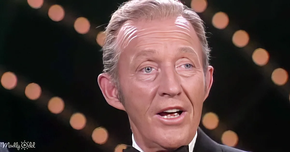 A man with short, light-colored hair and a black suit, smiling with his mouth slightly open.