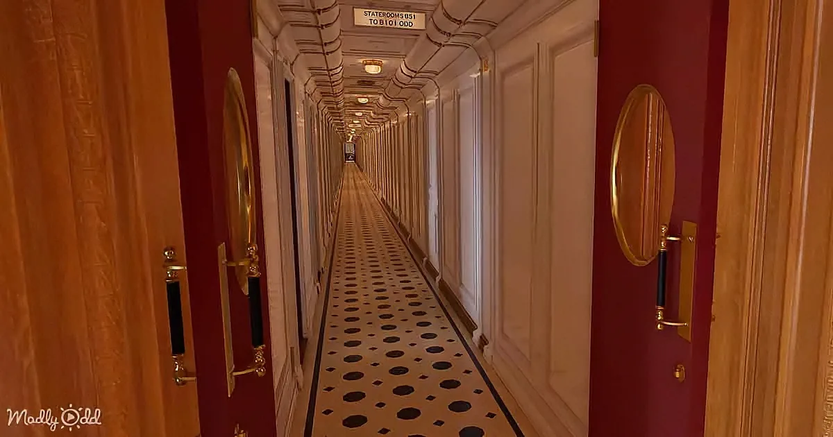 A long, elegant hallway with red walls, white doors, and a patterned floor leads to staterooms.