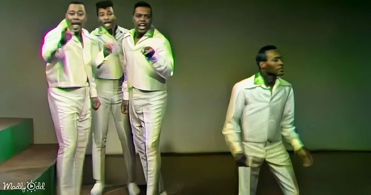 Four men in white suits with green accents are singing and dancing on stage.