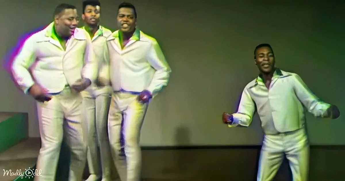 Four men in white suits with green accents are dancing on stage.