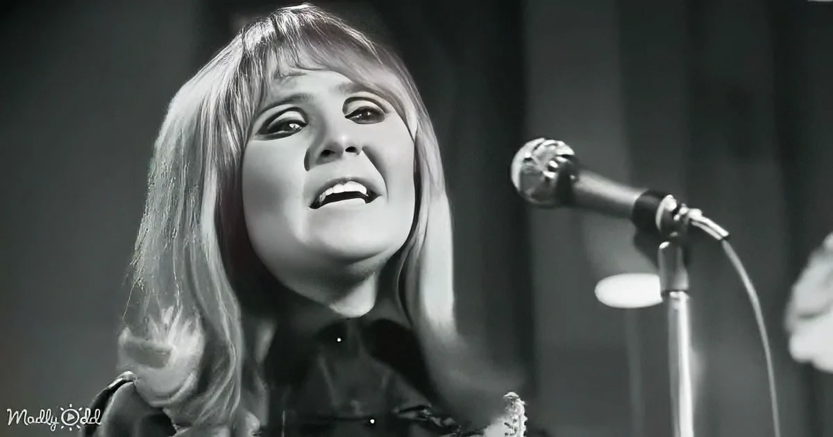 A woman with long hair sings into a microphone, her expression animated, in a black-and-white image.