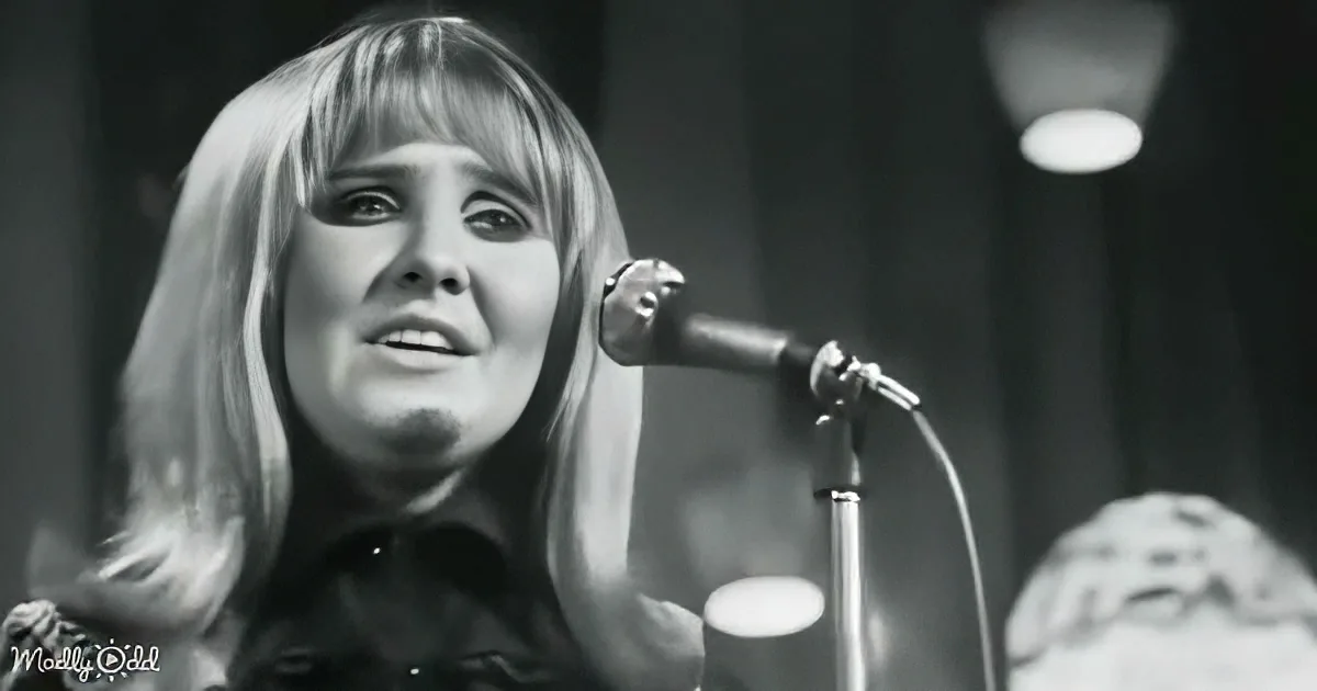 A woman with long hair sings into a microphone, her expression focused, in a black-and-white image.