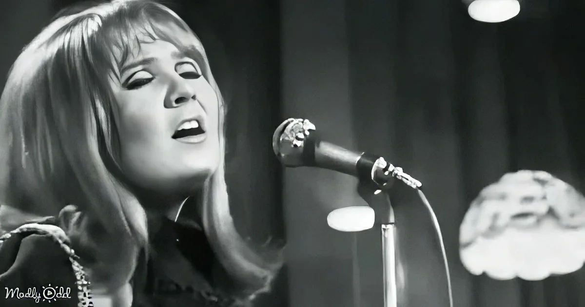 A woman with shoulder-length hair sings into a microphone, her eyes closed, in a black-and-white image.