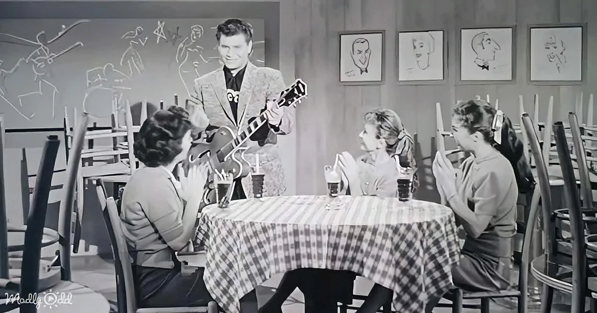 A man plays guitar on stage, captivating diners at a checkered tablecloth restaurant.