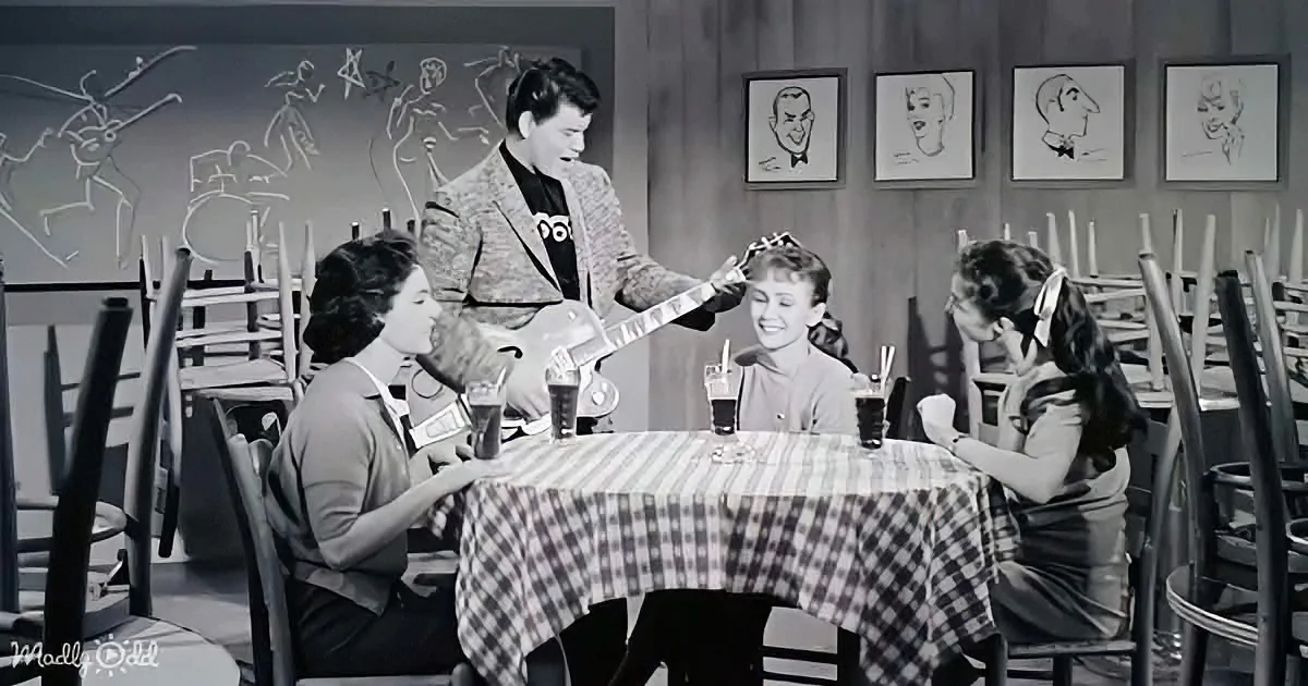 A man plays guitar for three women at a diner table, creating a lively atmosphere.