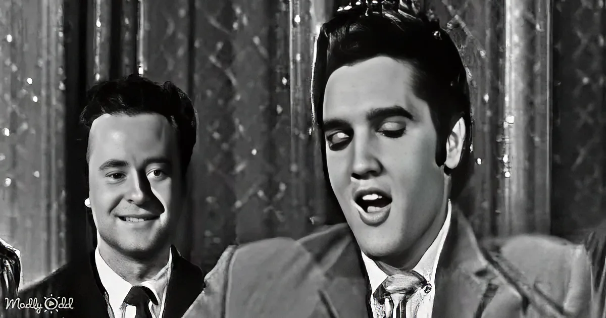 Elvis Presley sings passionately, wearing a suit, with another man smiling in the background.
