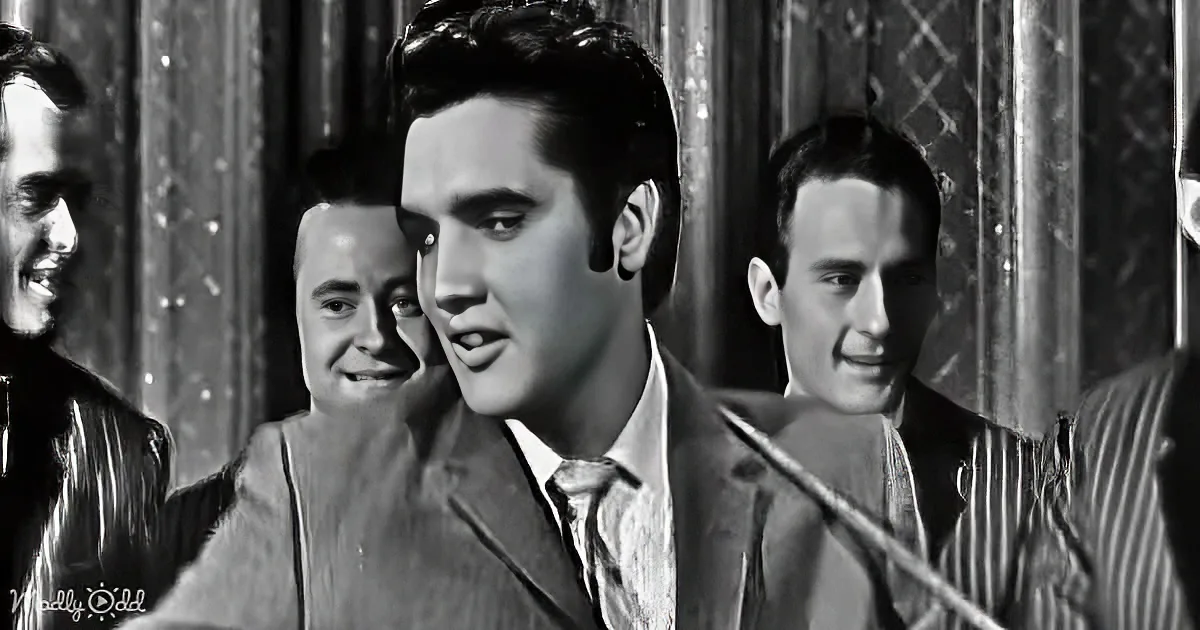 Elvis Presley in a suit, surrounded by smiling men, in a black-and-white scene.