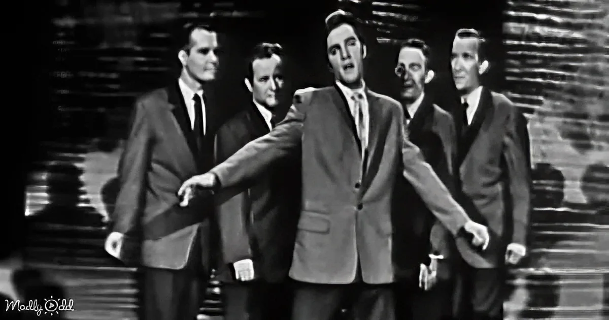 A man in a suit dances energetically in front of a group of similarly dressed men.