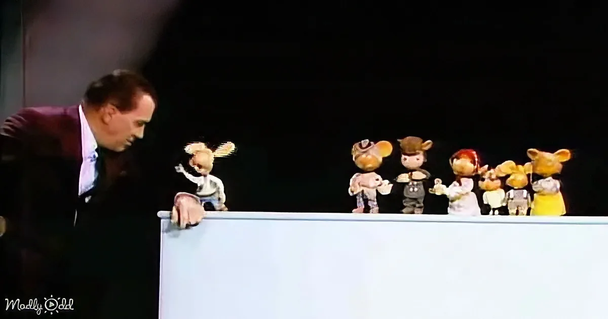 A man in a suit leans over a table, interacting with a row of colorful puppets.