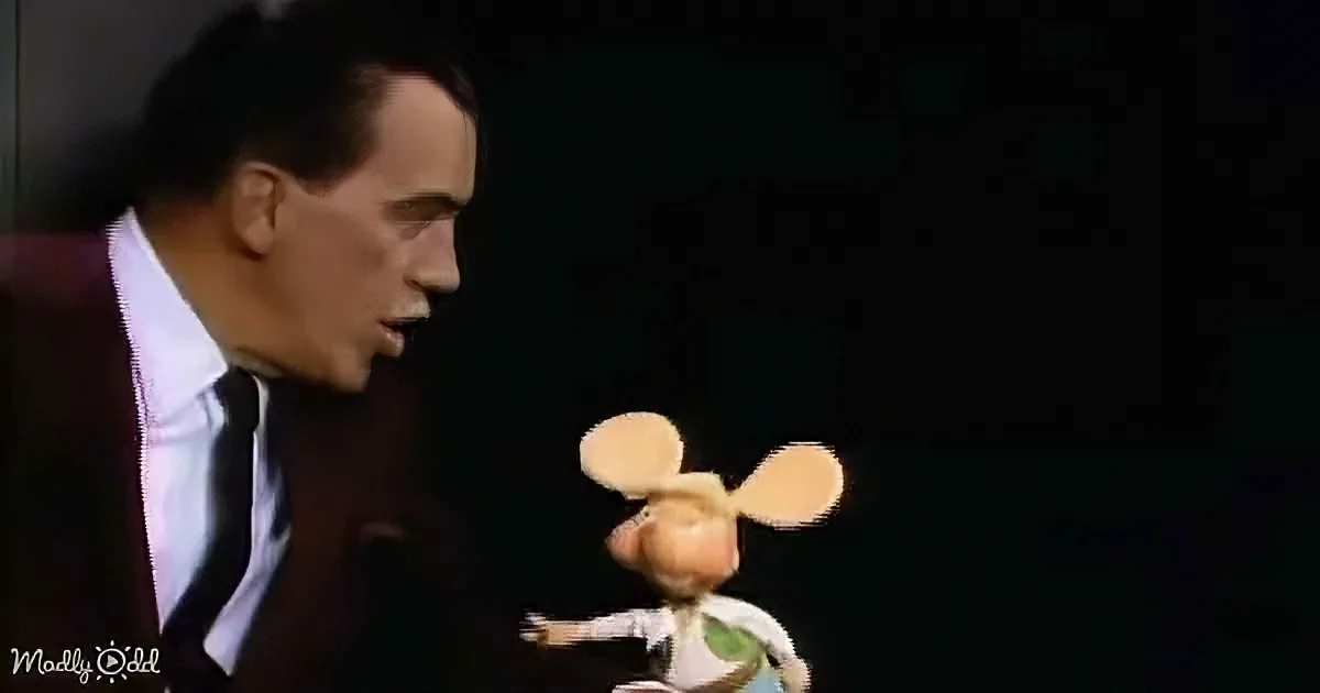A man in a suit and tie is holding a puppet with large ears and a green shirt.