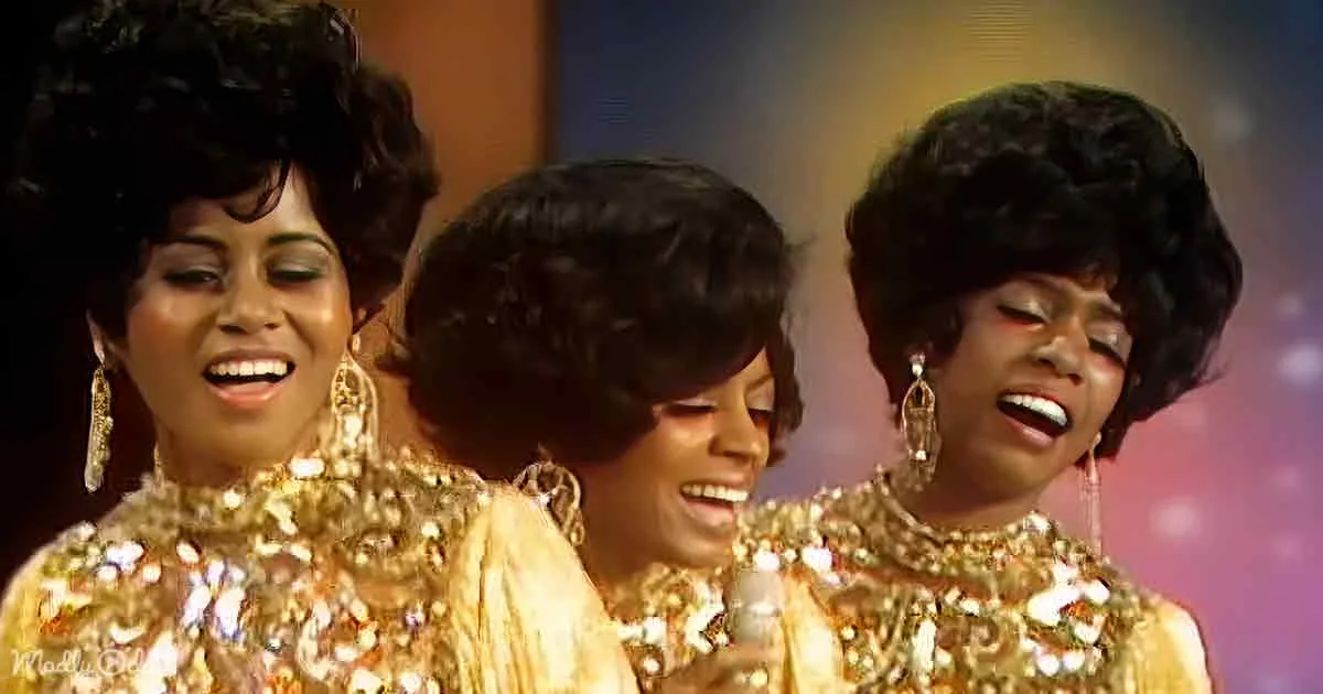 Three women in shimmering gold outfits, smiling and singing together, creating a vibrant and joyful scene.