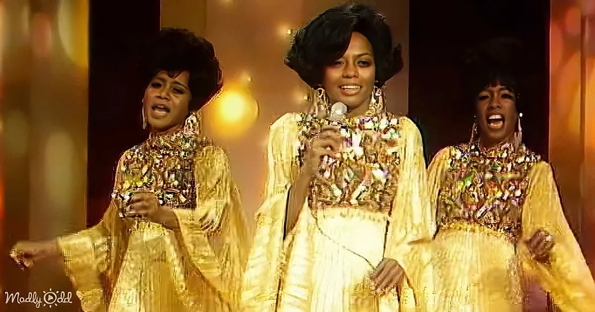 A woman in a gold sequined dress sings passionately on stage with a microphone.