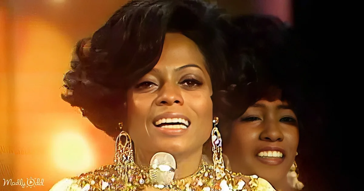A woman with a large afro hairstyle, wearing ornate jewelry, sings into a microphone.