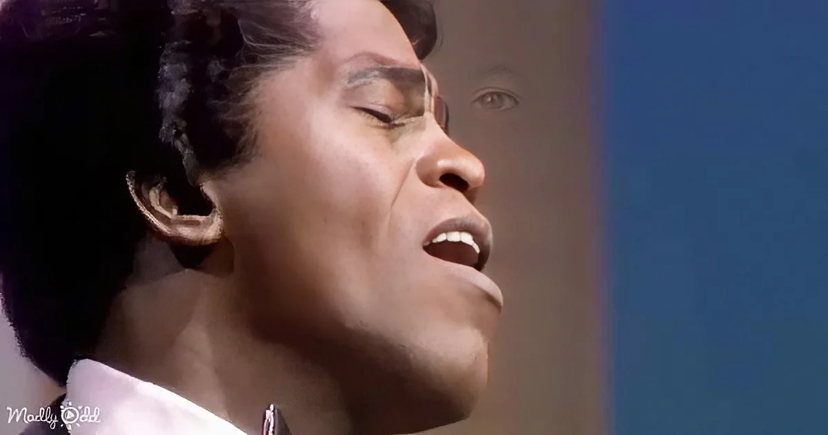 A person with closed eyes and an open mouth, possibly singing or speaking, wearing a white shirt.