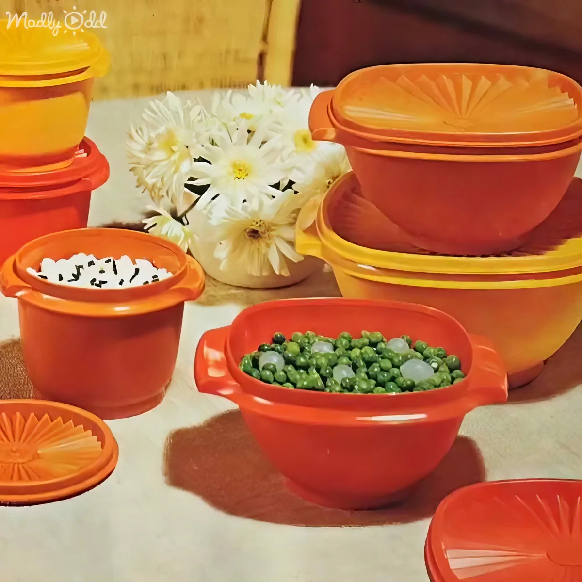 Vibrant orange Tupperware containers with peas, rice, and flowers on a table.