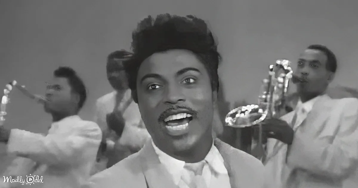 A man in a suit sings passionately in front of a band playing brass instruments.