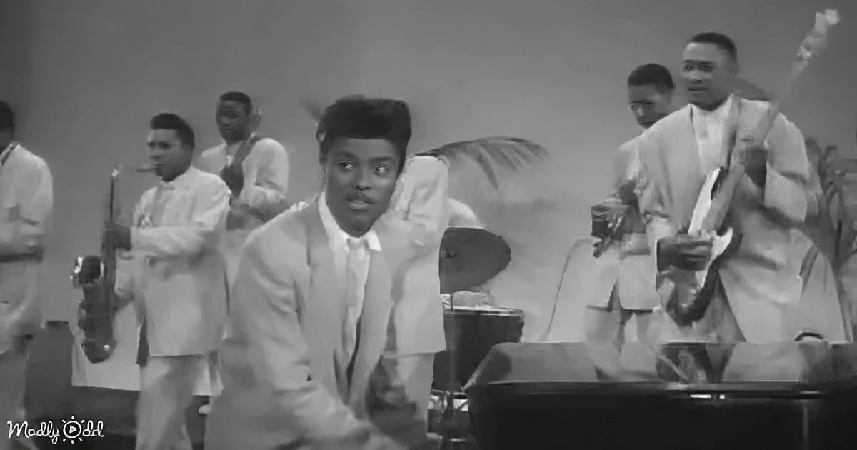 A man in a suit sits at a piano, surrounded by musicians in a vintage setting.