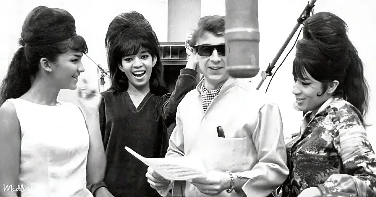 A man in sunglasses holds a paper, surrounded by three smiling women with 1960s hairstyles.