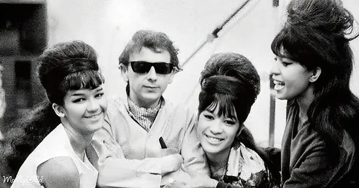 A man in sunglasses and three women with 1960s hairstyles smile together, possibly from a music group or film.
