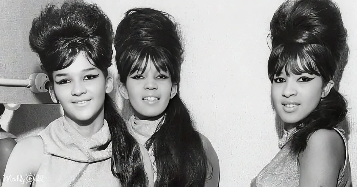 Three women with 1960s hairstyles, wearing dresses, posing together in a black-and-white photo.