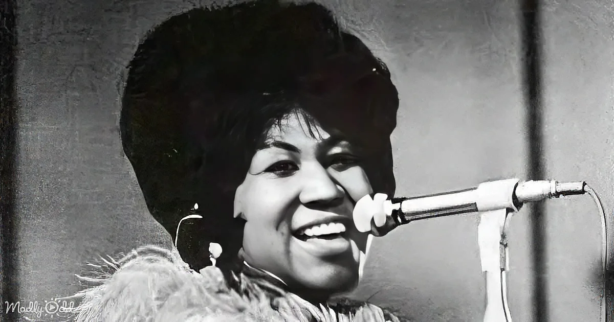 Aretha Franklin smiles while singing into a microphone, wearing a fur coat and large earrings.