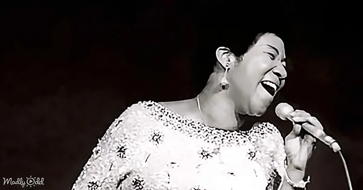 A woman in a floral dress sings passionately into a microphone, her face illuminated against a dark background.