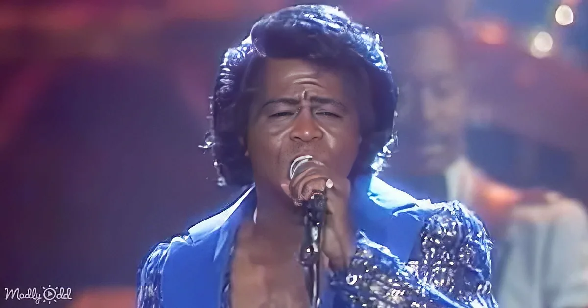 A person in a blue, sparkly outfit sings into a microphone on stage.