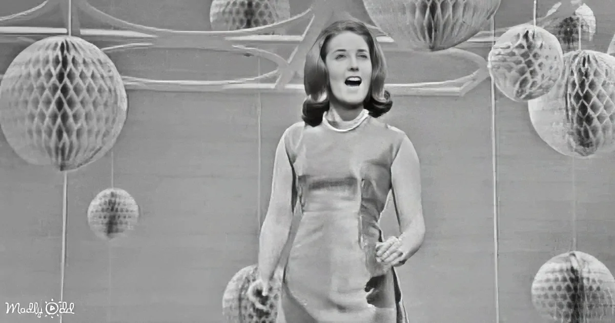 A woman in a 1960s dress stands in front of a wall with hanging paper decorations.