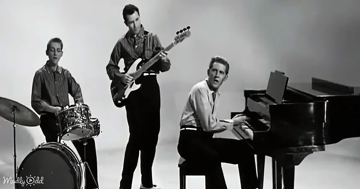A man plays piano while another sings, with a guitarist and drummer in the background.