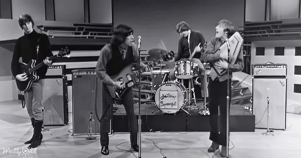 A band performs with guitars, drums, and a harmonica in a recording studio setting.