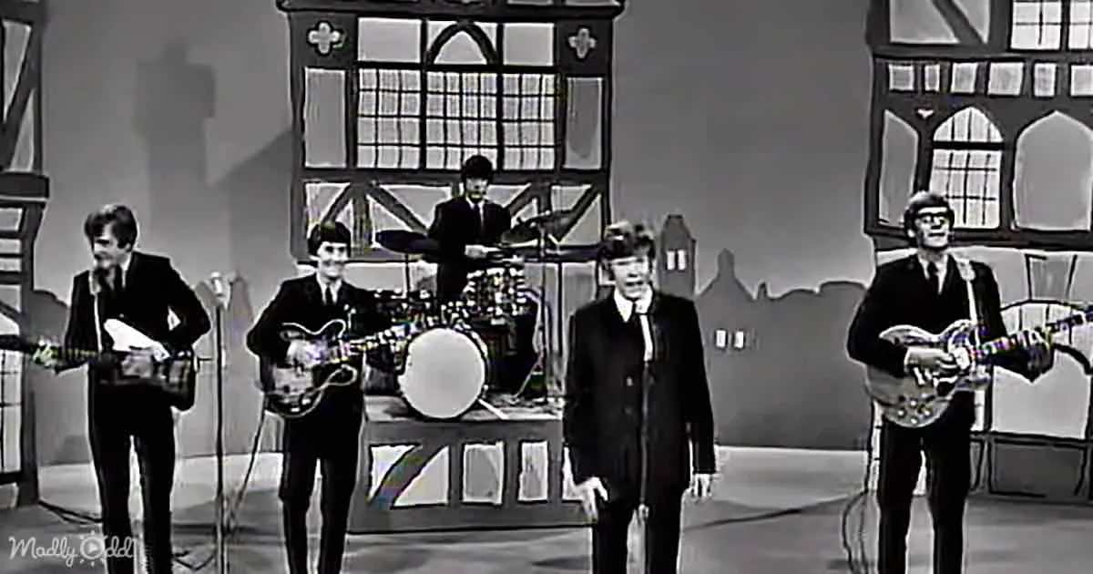 The Beatles perform on stage with guitars, drums, and microphones, dressed in suits.