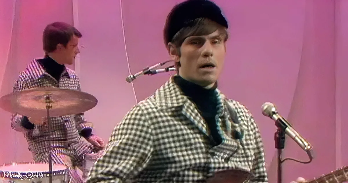 A man in a checkered suit sings into a microphone, with another man playing drums in the background.