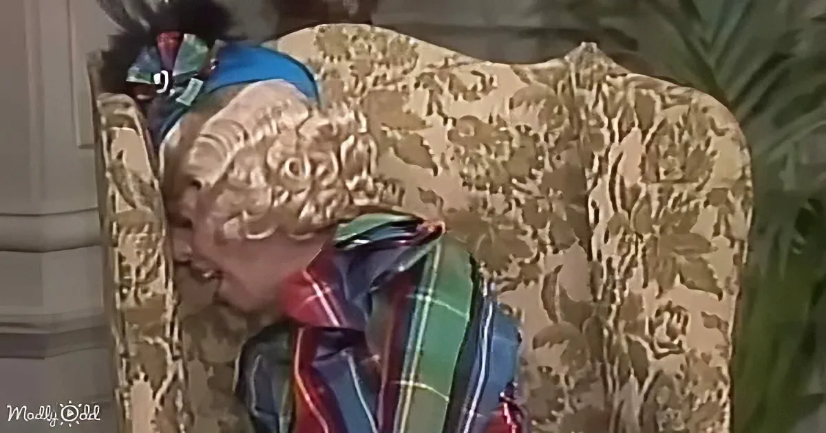 A person with curly hair and a colorful headband leans against a floral-patterned chair.