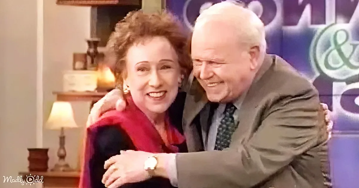 An older couple embraces warmly, smiling, in a cozy indoor setting.