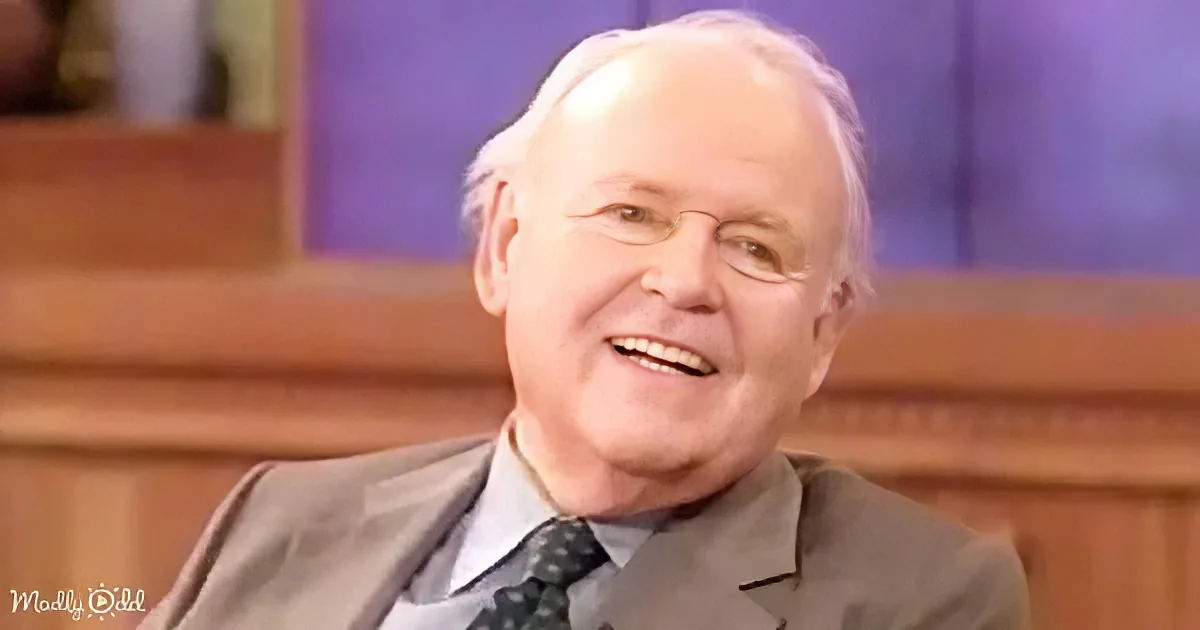 A smiling older man in a suit and tie, sitting in a studio setting.