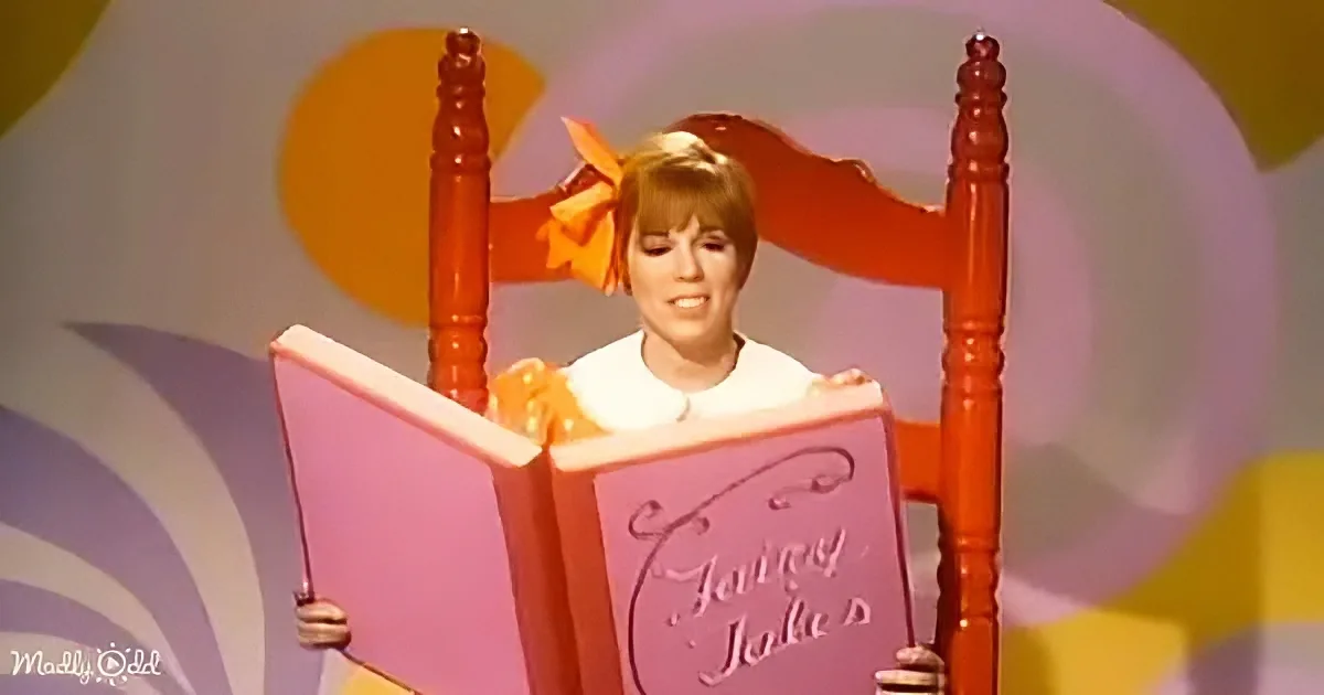 A person in a white dress sits in a red chair, holding a large pink book titled "Fairy Tales."