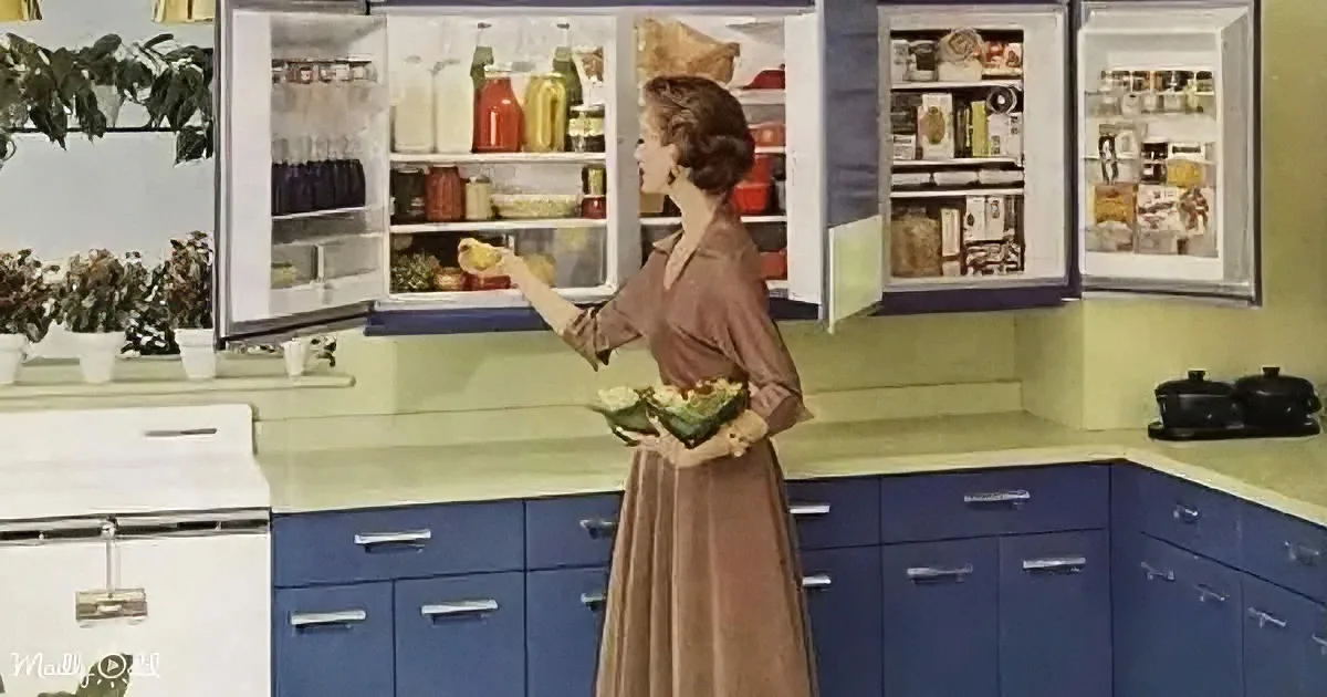A woman in a brown dress stands in a retro kitchen, holding bananas, with a fully stocked refrigerator and blue cabinets.