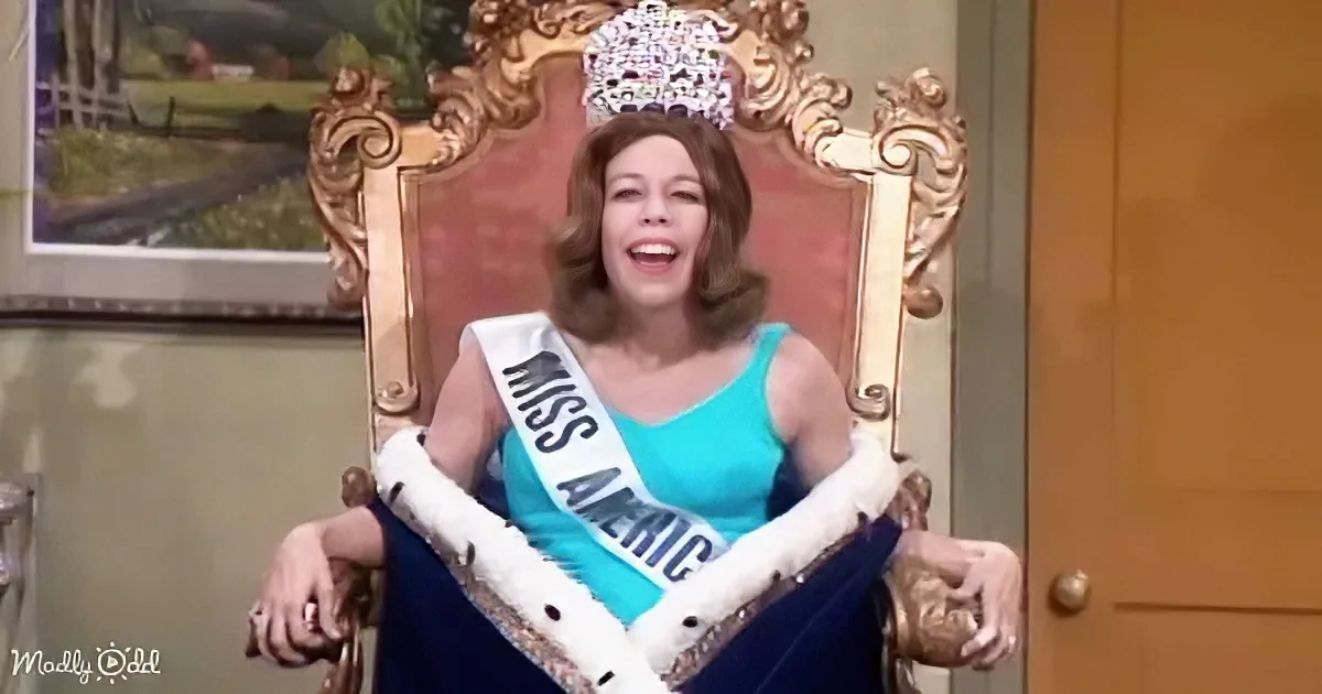 Woman in teal dress, "Miss America" sash, crown, sitting on ornate throne, smiling.