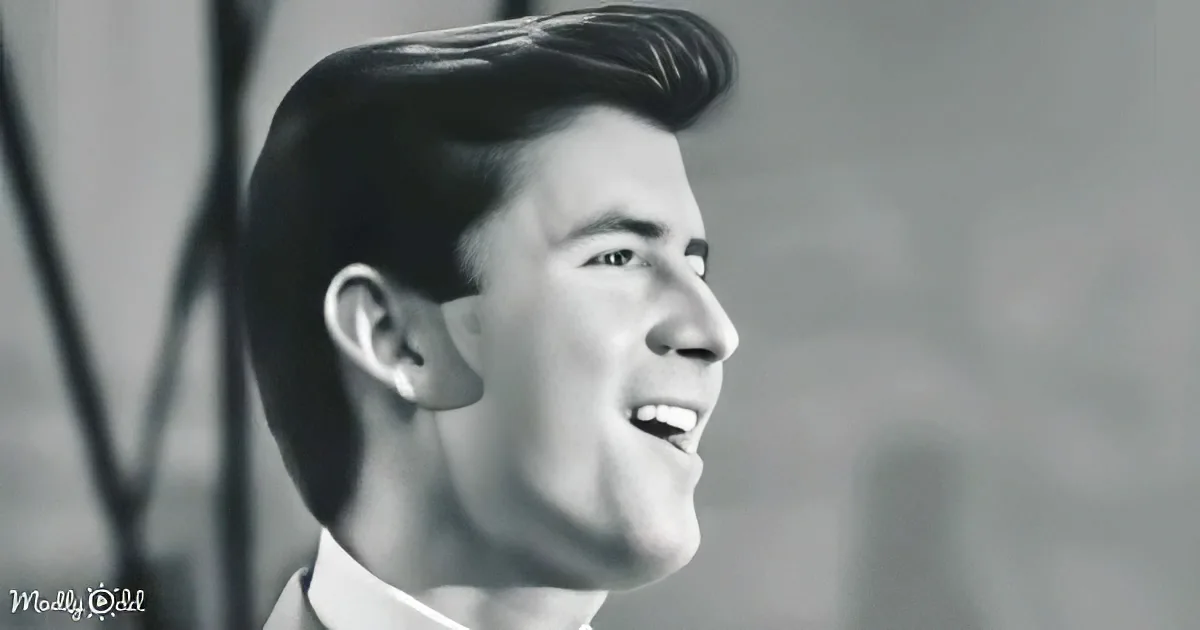 A man with a classic hairstyle and a white shirt is smiling in a black-and-white image.
