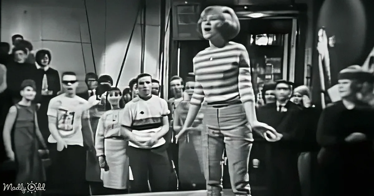 A young boy in a striped shirt stands in front of a crowd, appearing to sing or shout.