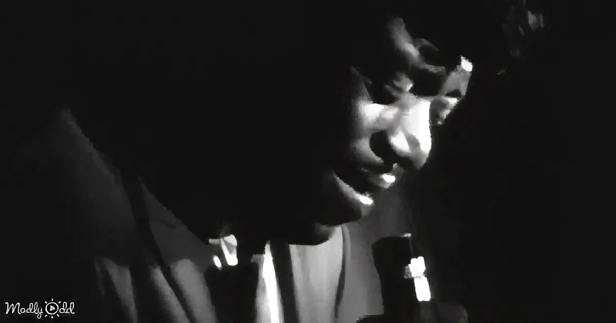 A person in a dark setting, illuminated by a light source, holding a microphone.