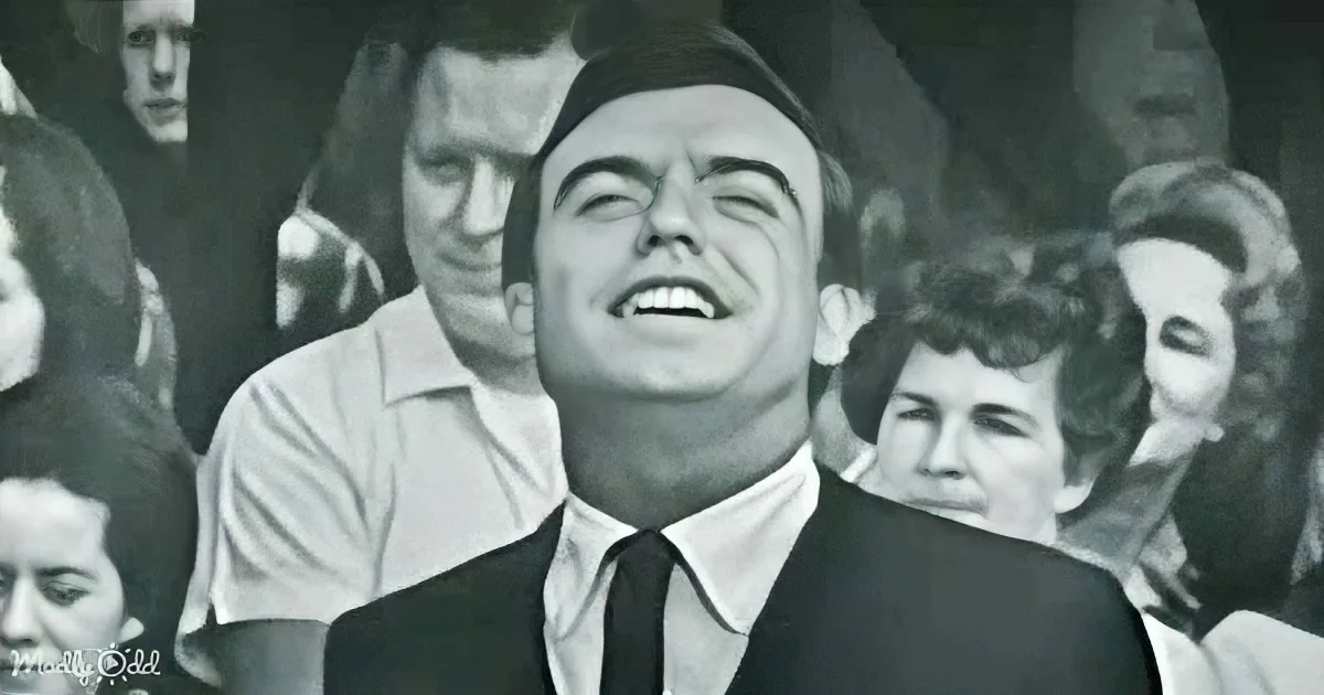A man in a suit and tie is laughing heartily in front of a crowd.