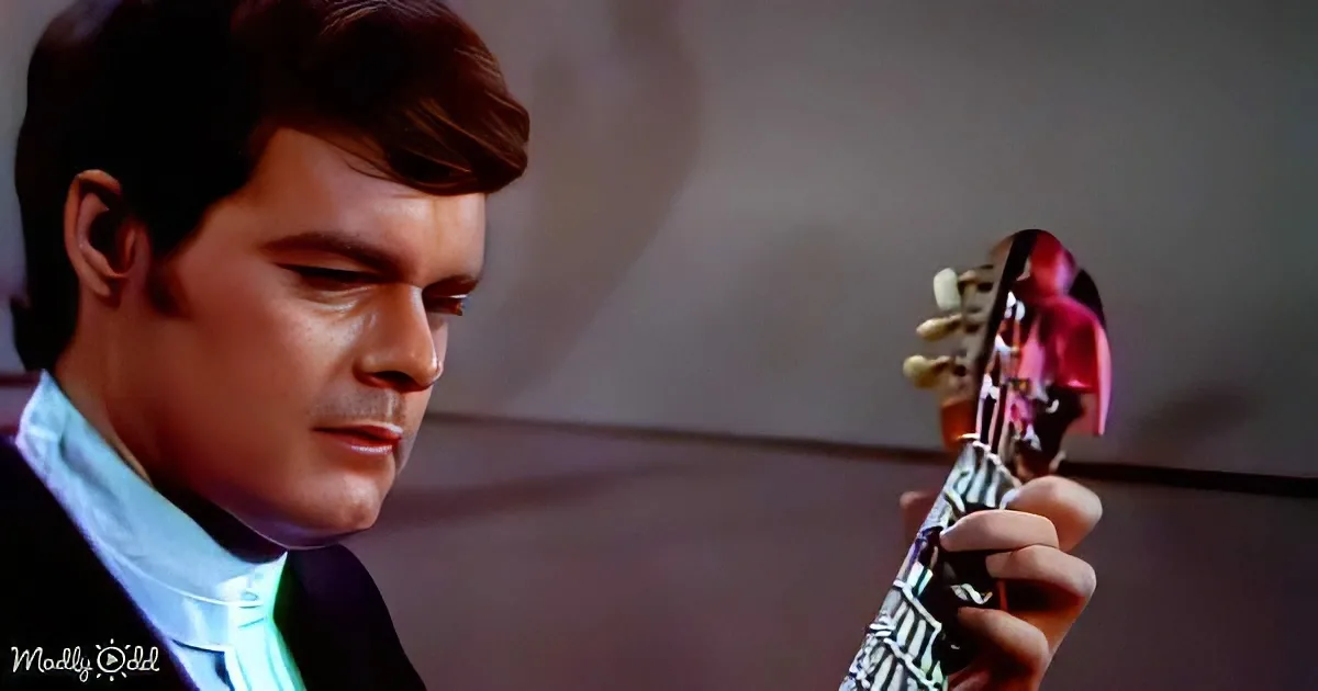 A man in a suit holds a violin, looking down with a serious expression.