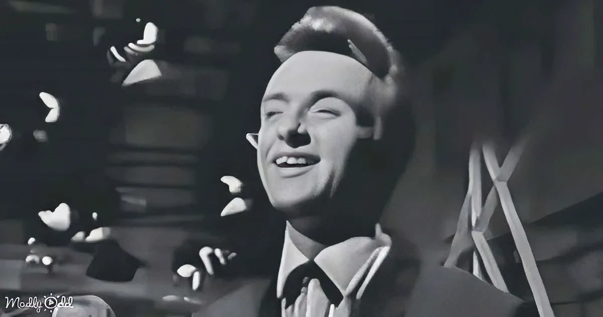A man in a suit and tie smiles widely, possibly singing, in a black-and-white scene.