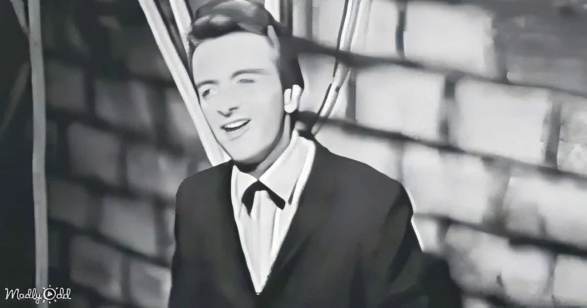 A man in a suit and tie smiles, standing in front of a brick wall.