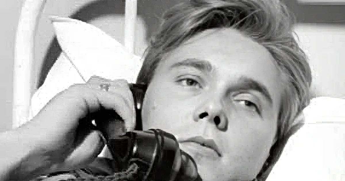 A man with short hair, wearing a dark shirt, is shown in a black-and-white close-up, looking slightly to the side.